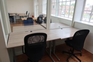 Twee werkplekken met bureaustoelen gescheiden door een glazen wand in een lichte kantoorruimte aan het Gedempt Hamerkanaal.